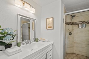A bathroom with a white vanity, a large mirror, a framed picture on the wall, and a shower area with a handheld showerhead. - Magnolia House w/ 4 Beds 2 Baths on 1.5 Acres ⭐ (Magnolia)