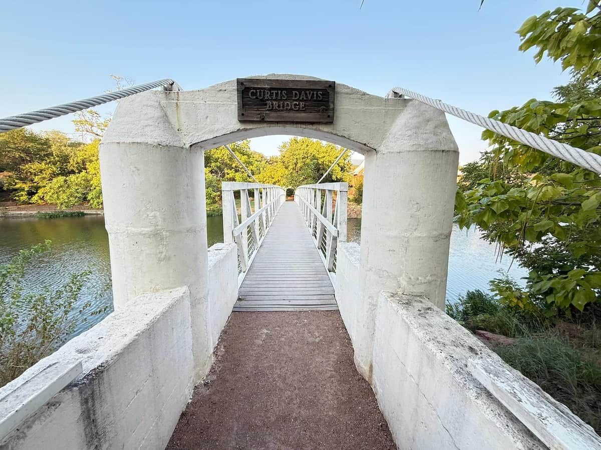 Eine Beton-Fußgängerbrücke mit einem Schild, auf dem 'CURTIS DAVIS BRIDGE' steht, führt zu einem Gewässer.