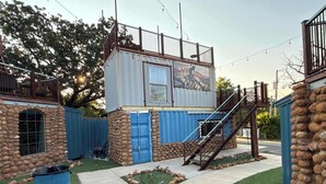 Uma cabana rústica com fachada de pedra, uma porta azul e um pequeno alpendre com guarda-corpo.