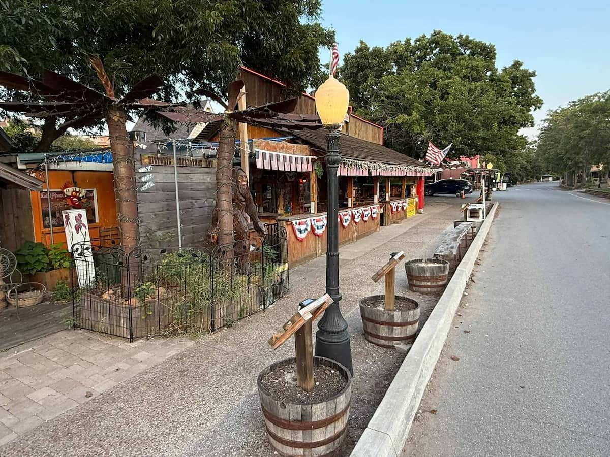 A street with a wooden building, a fence, and barrels.
