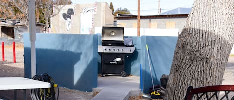 An outdoor barbecue area with a grill, tables, and a tree.
