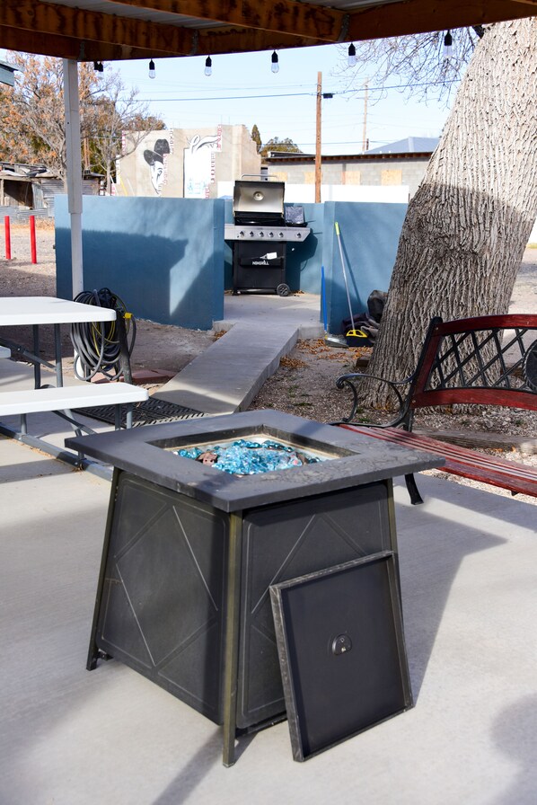 An outdoor barbecue area with a grill, tables, and a tree.