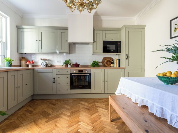 A kitchen with light-colored cabinets, a wooden herringbone floor, a built-in oven, and a microwave.