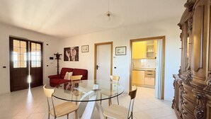 Ein Essbereich mit einem Glastisch und Stühlen, einem roten Sofa und einer Küche im Hintergrund.