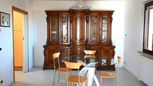 Ein Essbereich mit einem runden Glastisch, Holzstühlen und einer großen Holzvitrine mit Glastüren.