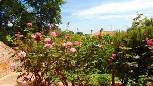 Ein Garten mit blühenden rosa Rosen, einer Ziegelmauer und einem Gebäude mit einem Ziegeldach im Hintergrund.