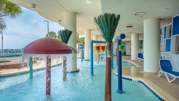 Indendørs pool med vandfald, palmer og liggestole.