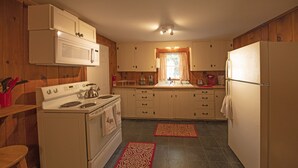 A compact kitchen with wooden cabinets, a white stove, and a refrigerator. - Hideaway Cottages, Cottage B (New London)