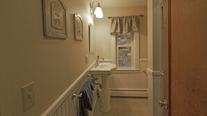 A narrow hallway with a bathroom at the end, featuring a sink, mirror, and window with a view. - Hideaway Cottages, Cottage B (New London)