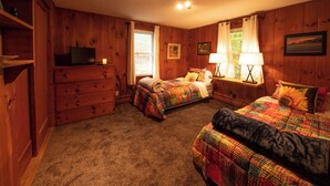 A cozy bedroom with two beds, a dresser, a television, and a window with curtains. - Hideaway Cottages, Cottage B (New London)