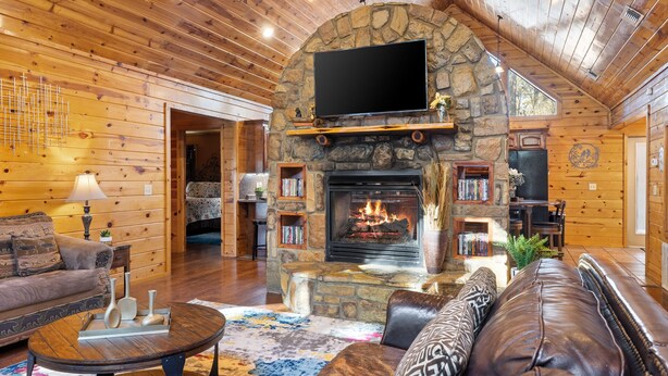 A cozy log cabin interior with a stone fireplace, wooden walls, and a comfortable seating area.
