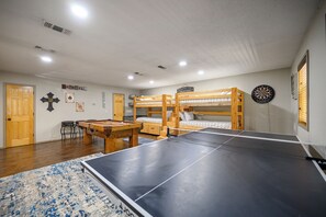 A room with bunk beds, a ping pong table, a dartboard, and a pool table.