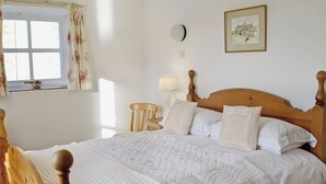 A neatly made bed with a wooden headboard, a bedside table, a lamp, and a window with floral curtains. - 4 bedroom accommodation in Grassington (Grassington)