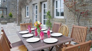 A wooden dining table set for six with white plates, pink napkins, and a vase of flowers. - 4 bedroom accommodation in Grassington (Grassington)