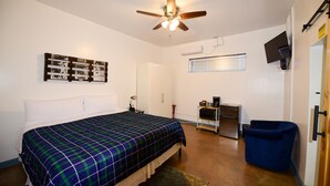 Un dormitorio con cama, ventilador de techo, escritorio con computadora, una silla y televisor montado en la pared.
