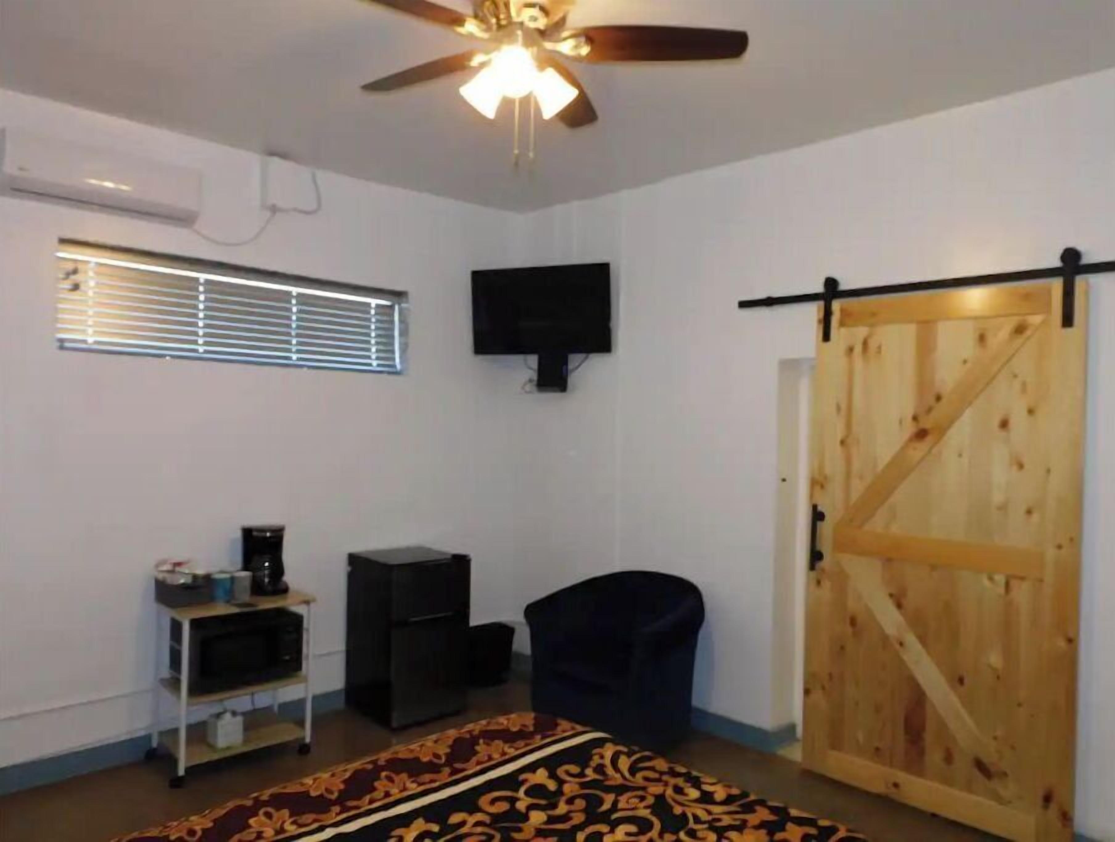 A room with a ceiling fan, a mounted TV, a sliding barn-style door, a small black chair, and a shelf with a speaker and other items.