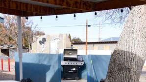 An outdoor barbecue area with a grill, tables, and a tree. - Carmen's Marfa Hotel/Leticia 2 Queen Beds (Marfa)