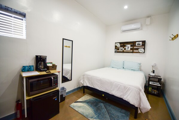 Un dormitorio con cama, microondas, refrigerador, espejo y aire acondicionado instalado en la pared.