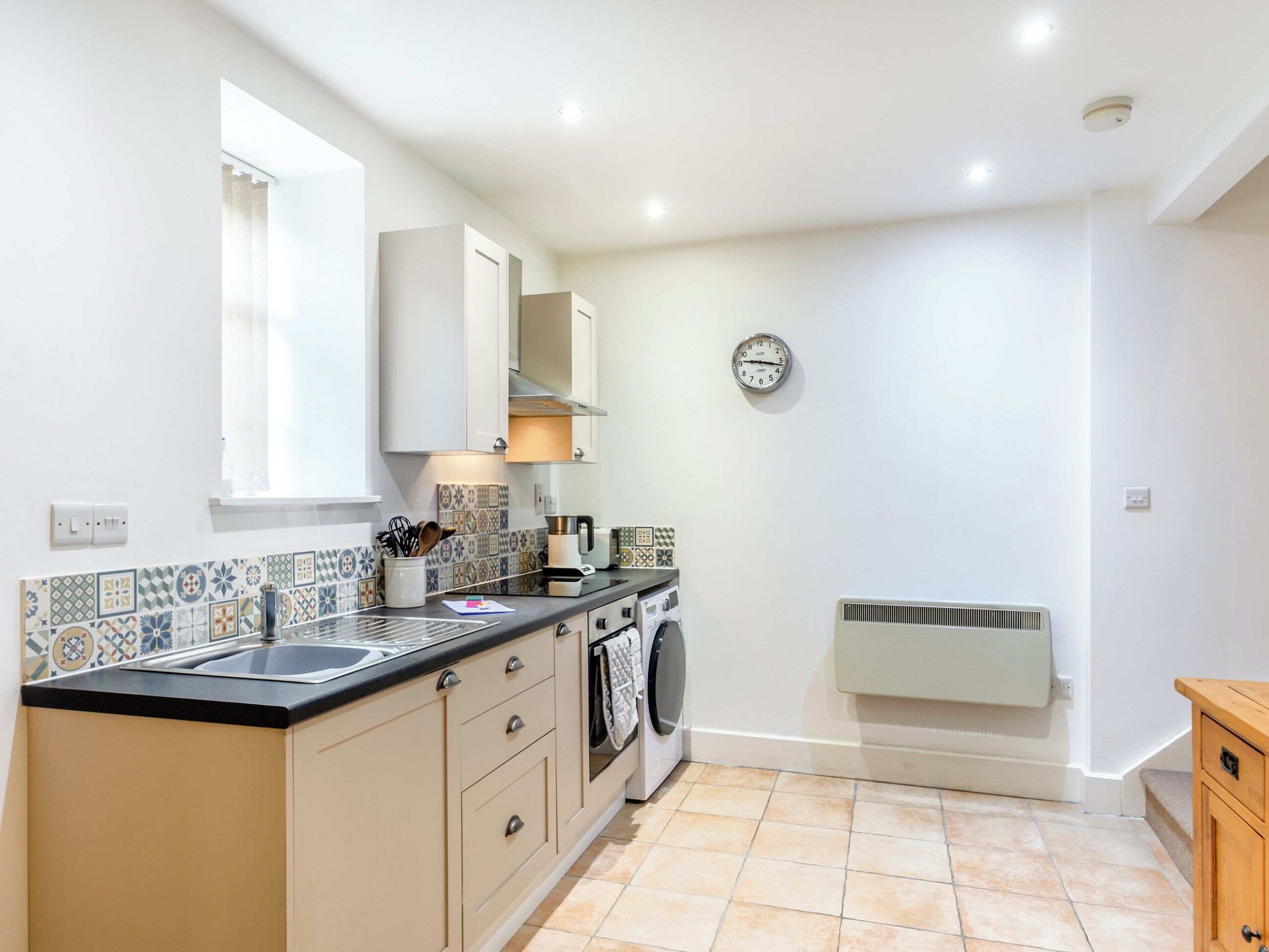 A compact kitchen with a sink, stove, and microwave, a washing machine, and a radiator.