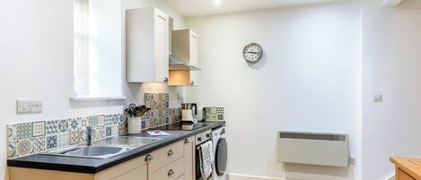 A compact kitchen with a sink, stove, and microwave, a washing machine, and a radiator.