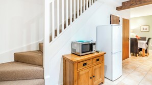 Una escalera con barandillas blancas, un armario de madera con cajones, un microondas y un refrigerador en un área de cocina.