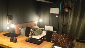 A modern bedroom with a wooden desk, a bed with a patterned bedspread, and a large window with curtains. - L'Ange de Fer (Illoud)