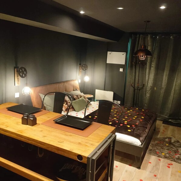 A modern bedroom with a wooden desk, a bed with a patterned bedspread, and a large window with curtains.