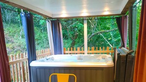 A hot tub with a wooden table and chairs, surrounded by curtains and a wooden fence, with a view of greenery outside. - L'Ange de Fer (Illoud)