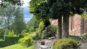 A stone staircase leading up to a stone wall, surrounded by lush greenery and trees.