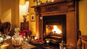A warmly lit fireplace with a clock above it, surrounded by various decorative items and a cozy seating area.