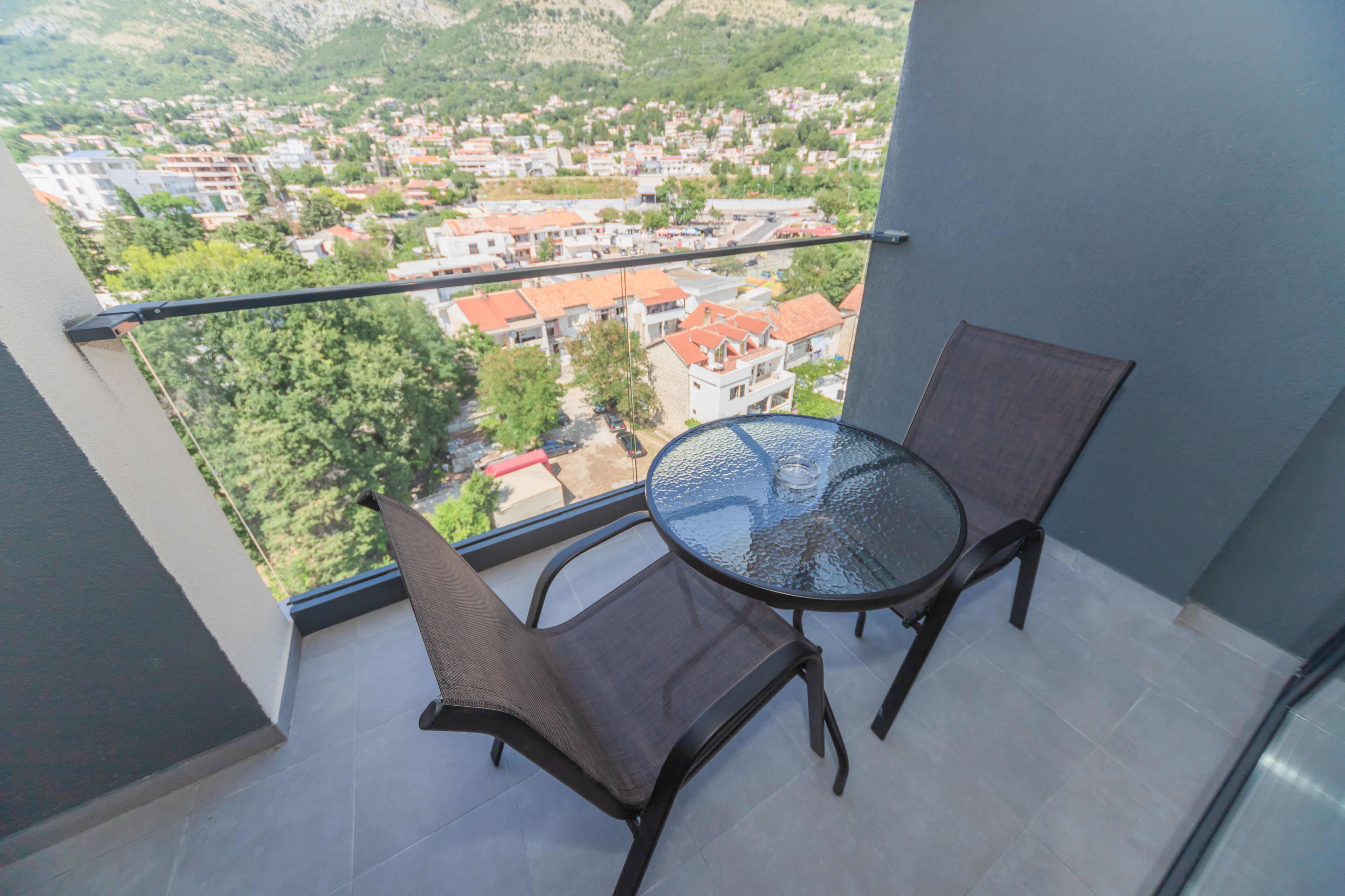Un balcón con una mesa de vidrio y dos sillas, con vista a una zona residencial con casas y vegetación.