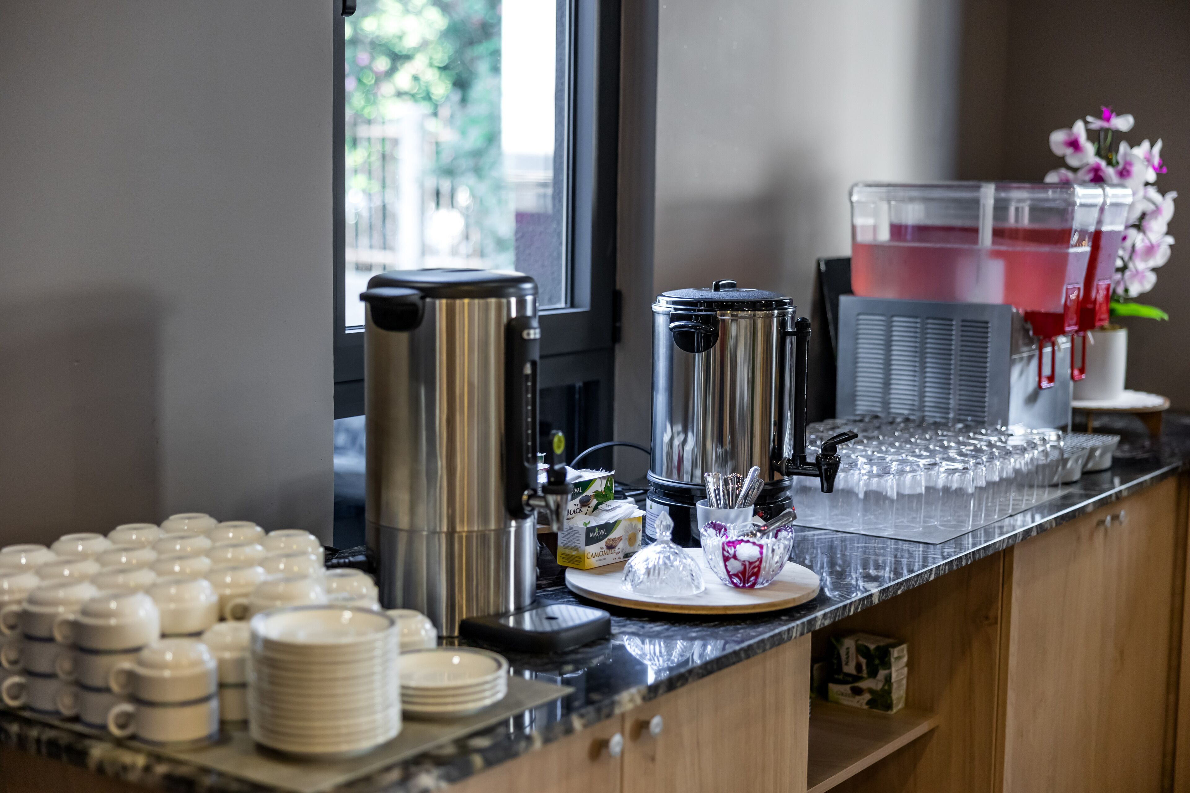 Una estación de café con varias cafeteras, un dispensador de agua y una variedad de tazas y platos.