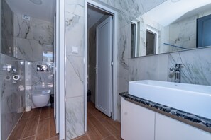 A modern bathroom with a white sink, marble walls, and a shower area. - N Hotel (Sutomore)