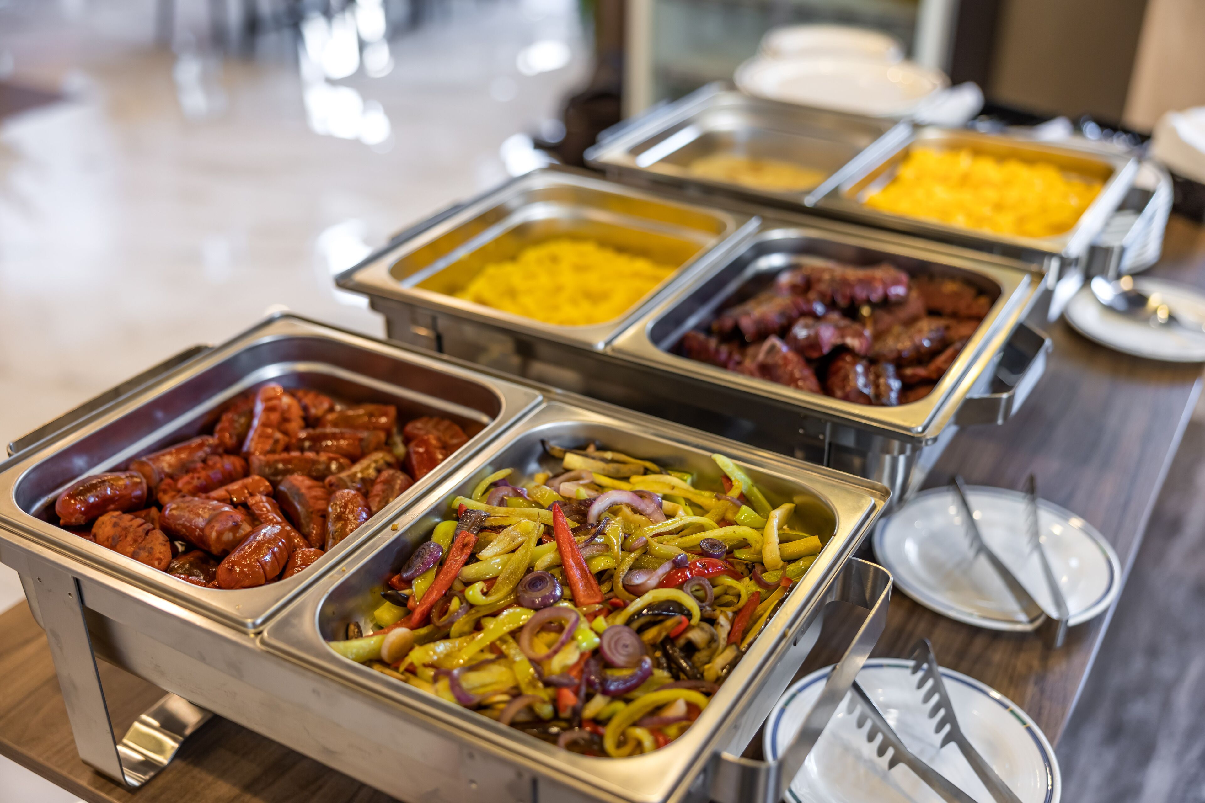 Buffet com diversas opções de comida, incluindo salsichas, pimentões e outros pratos.