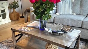 Ein Wohnzimmer mit Couch, Couchtisch, Lampe und einer Vase mit roten Blumen.