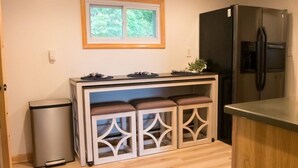 Eine kompakte Küche mit einem integrierten Kühlschrank, einer kleinen Mülltonne und einem Fenster über der Arbeitsfläche.