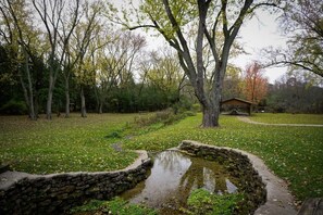 Ein Teich mit Steinverkleidung in einem Park mit Bäumen und einer Holzkonstruktion im Hintergrund.