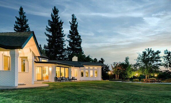 Une maison moderne dotée d’une grande véranda à l’avant, d’une pelouse bien entretenue et de grands arbres en arrière-plan.