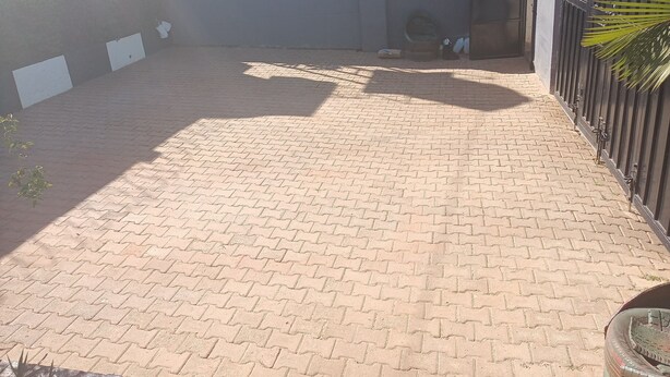 A paved courtyard with a brick pattern, a metal gate, and a building in the background. - Cozy b n' b in Bunga (Kampala)