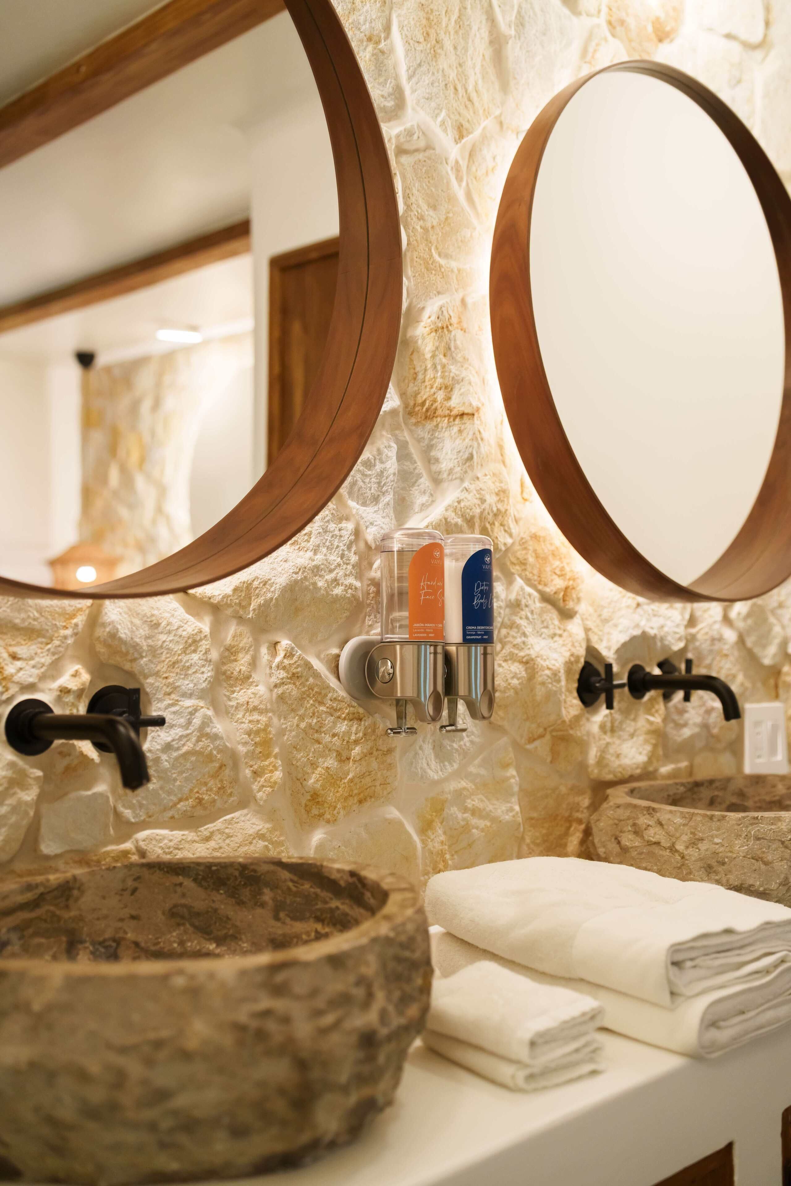 A bathroom with a stone wall, a wooden-framed mirror, a sink with a stone basin, and a towel rack.