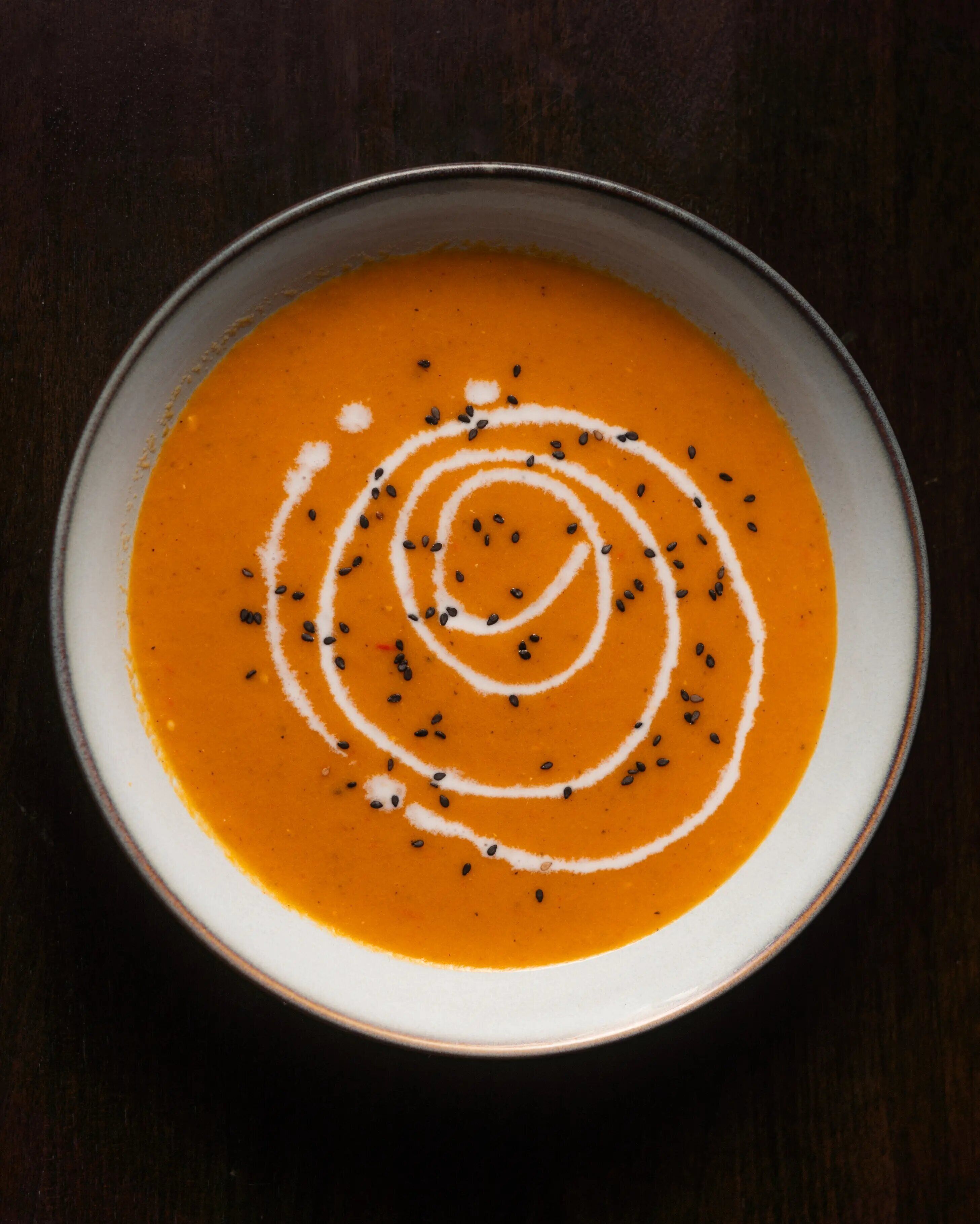 A bowl of soup with a swirl pattern and seeds on top.