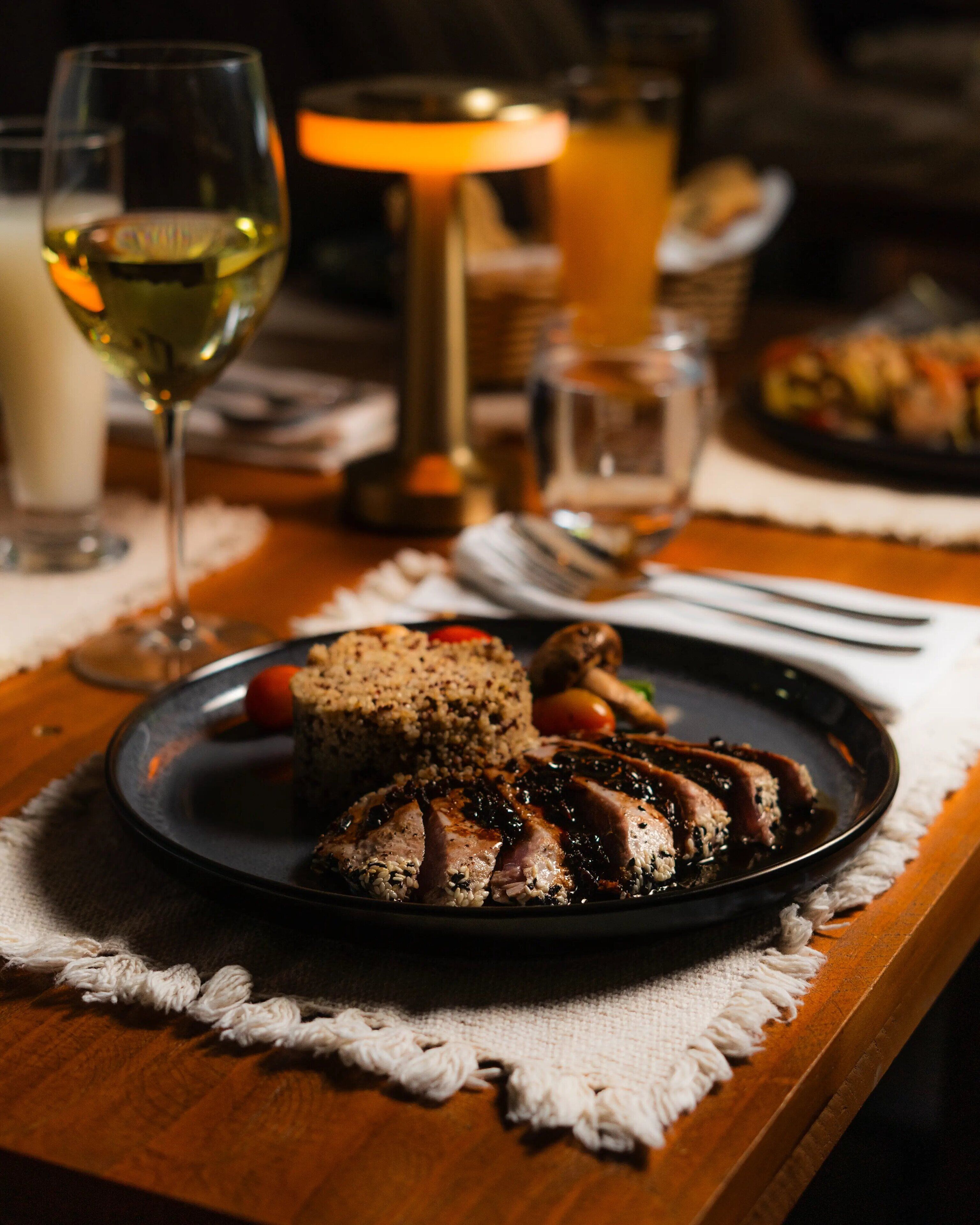 Una mesa de comedor con un plato de comida, una copa de vino blanco y una vela.