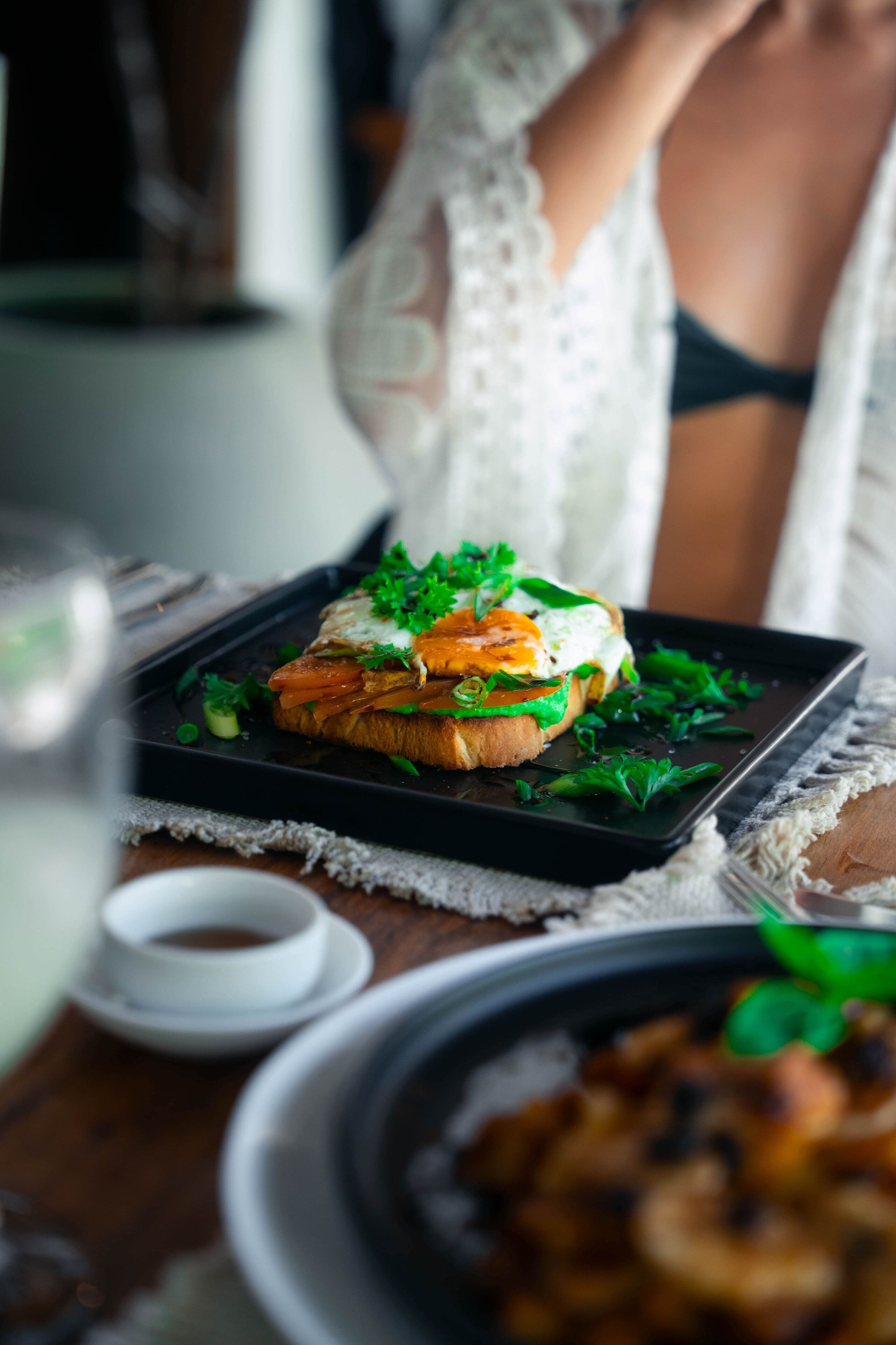 A meal with a sandwich on a black plate, garnished with greens, on a table with a white cloth.