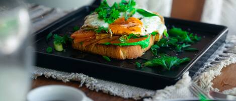 A meal with a sandwich on a black plate, garnished with greens, on a table with a white cloth.