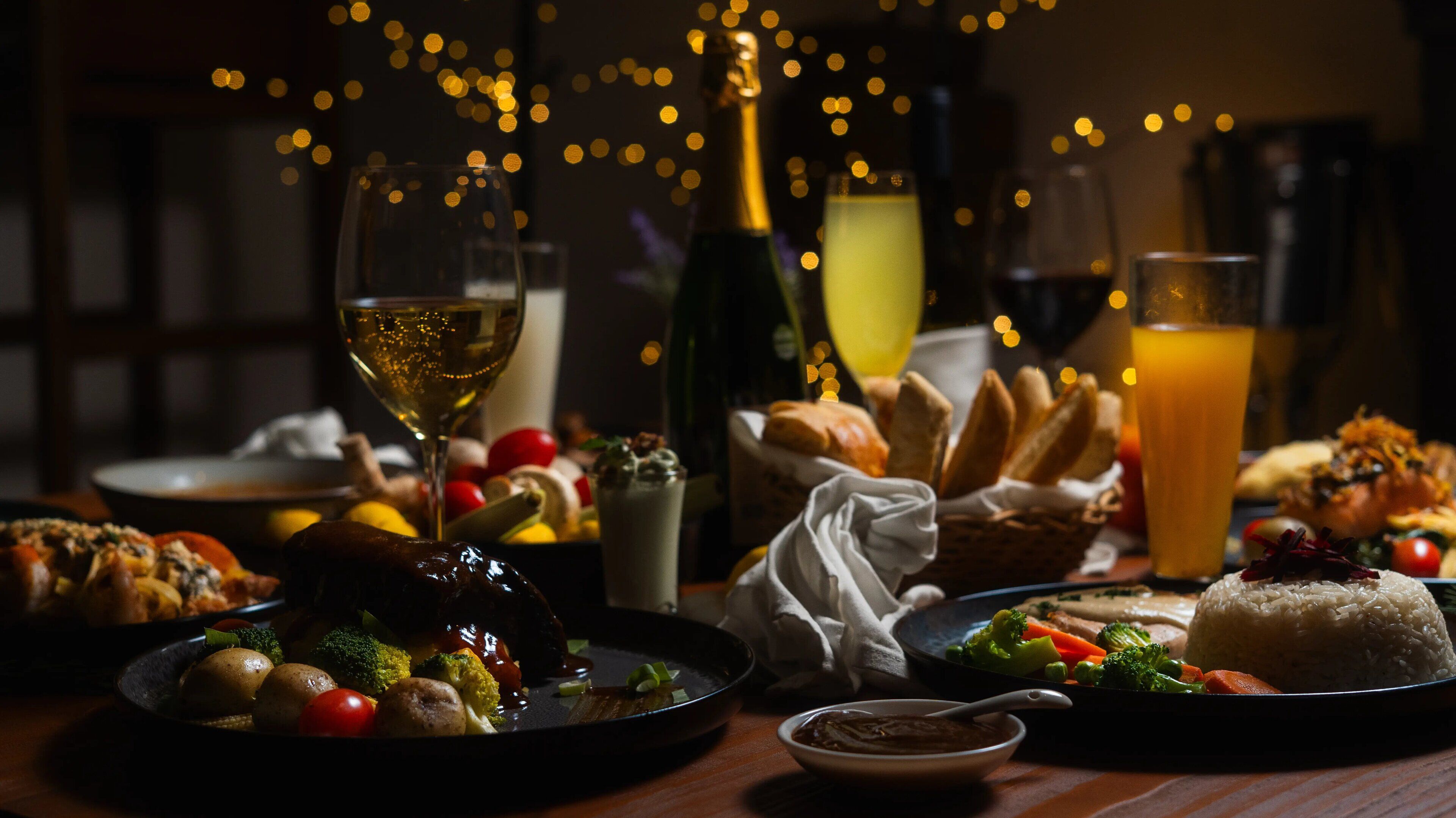 A dinner table with various dishes, including a steak, vegetables, and bread. There are also glasses of wine and a bottle of champagne.
