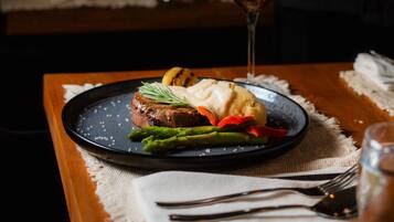 A dining table with a plate of food, a glass of red wine, and a person pouring wine.