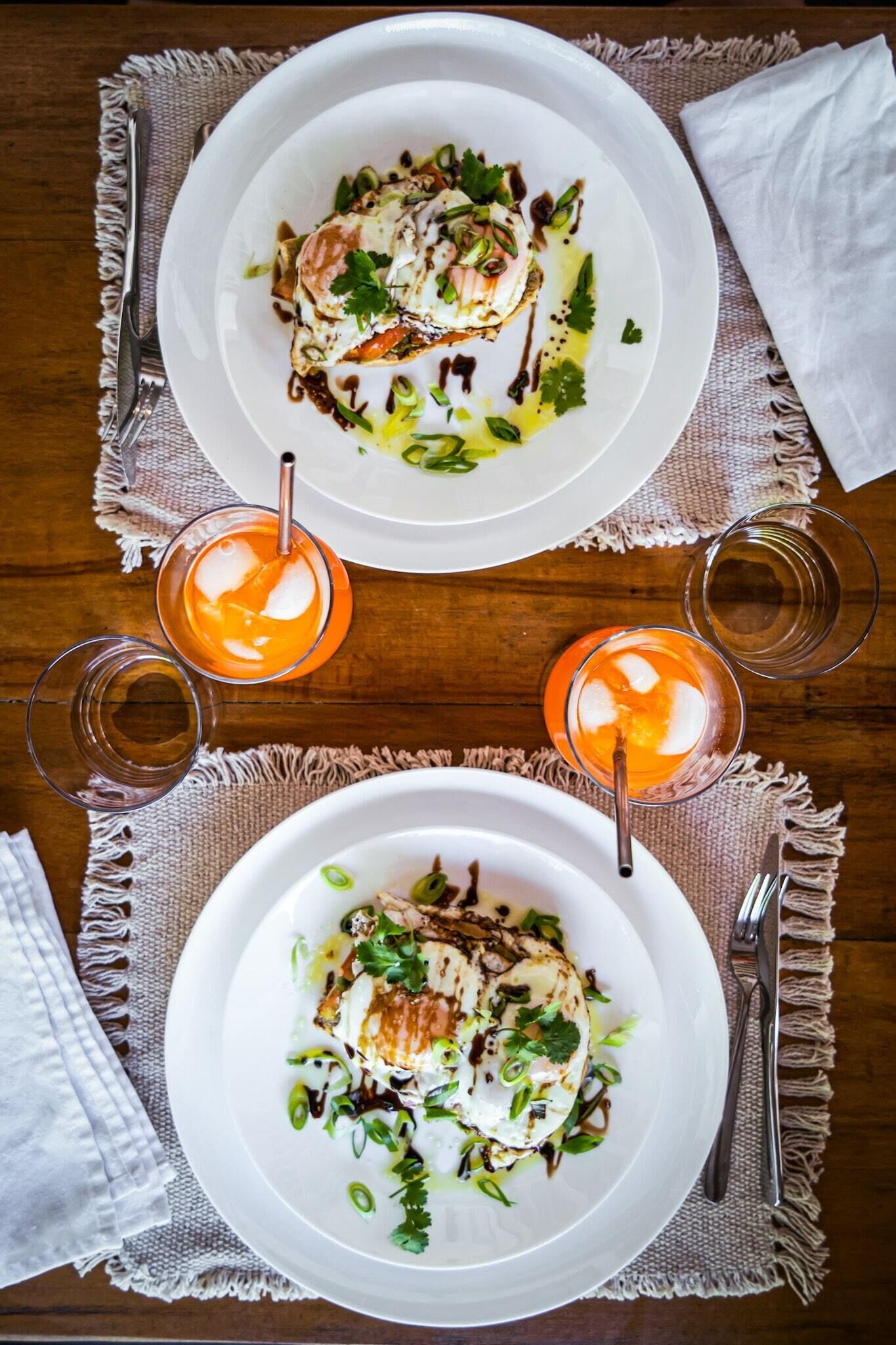Two white plates of food with garnishes, placed on a wooden table with a white cloth underneath.