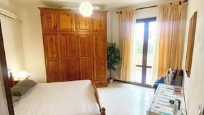 A bedroom with a bed, wooden wardrobe, a desk with a chair, and a potted plant. - Two-room apartment in Olbia (Olbia)