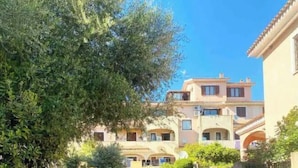 A narrow gravel path leading to a building with multiple balconies and a tiled roof. - Two-room apartment in Olbia (Olbia)