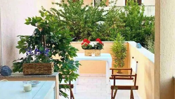 A balcony with a table and chairs, surrounded by lush greenery and a small flower arrangement. - Two-room apartment in Olbia (Olbia)